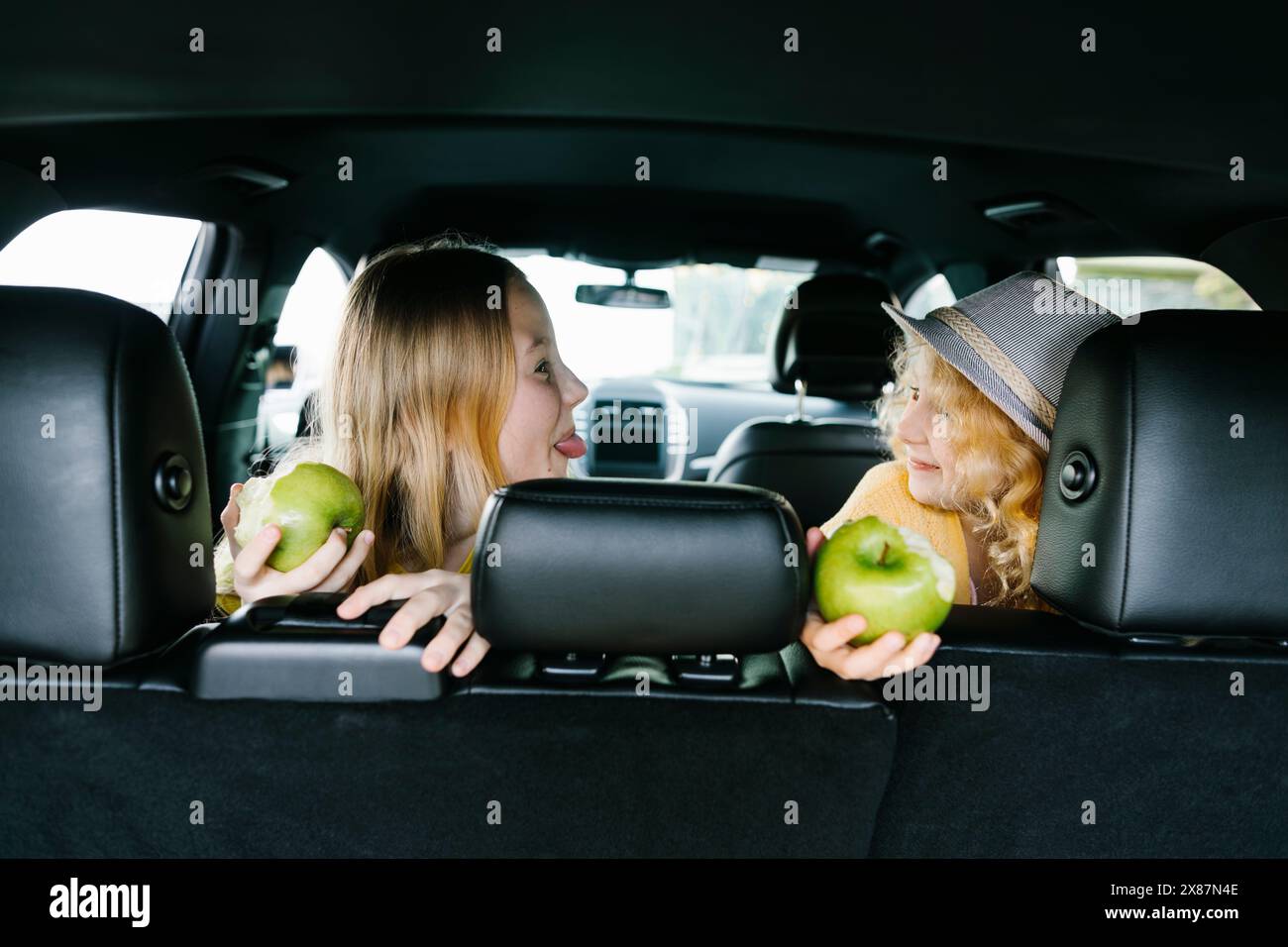 Playful sister holding half eaten apples in car Stock Photo