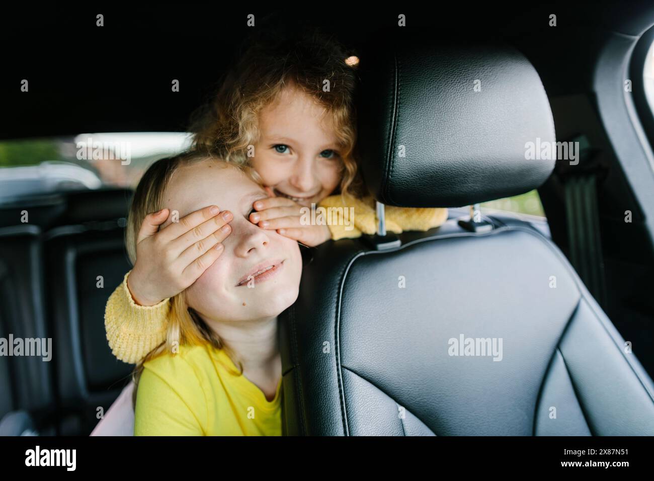 Girl covering eyes of sister in car Stock Photo