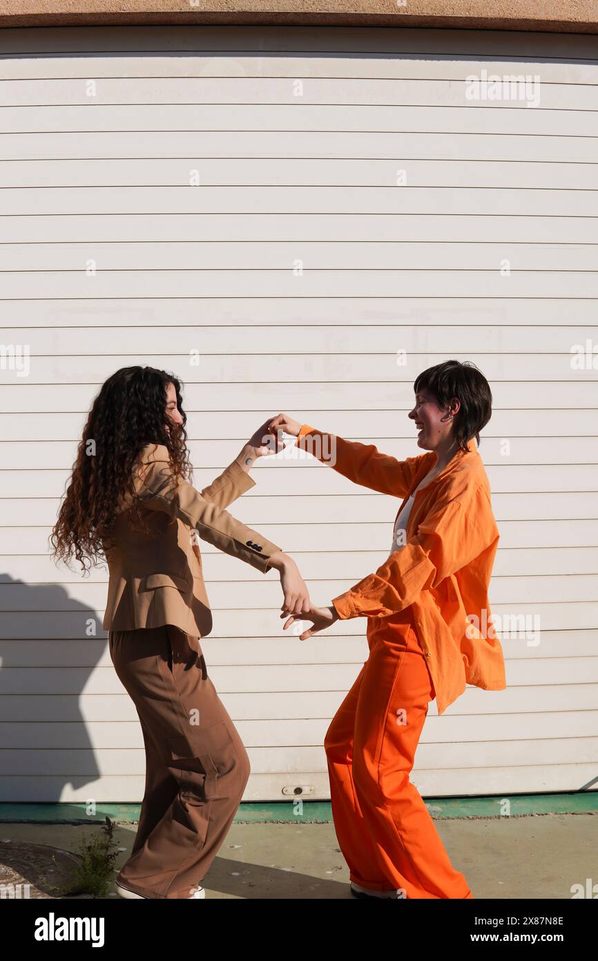 Happy lesbians holding hands dancing together in front of white wall Stock Photo