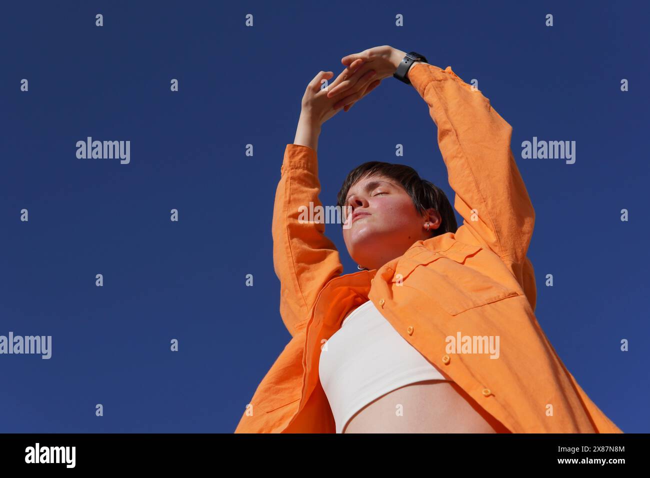 Woman in orange casuals with eyes closed under clear blue sky on sunny day Stock Photo