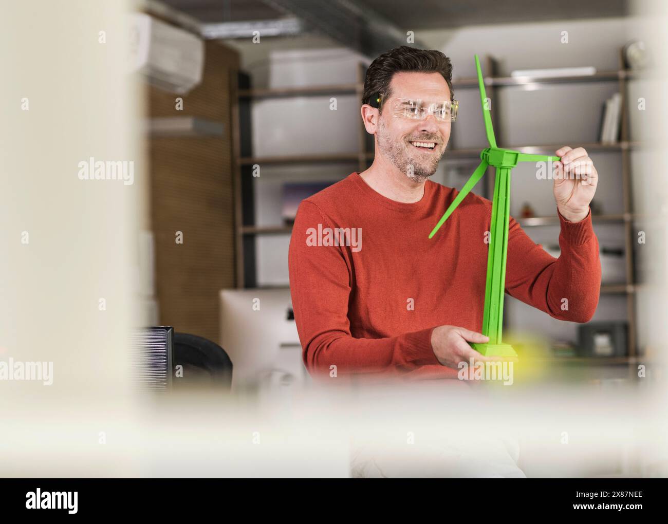 Smiling engineer examining green wind turbine model at office Stock Photo