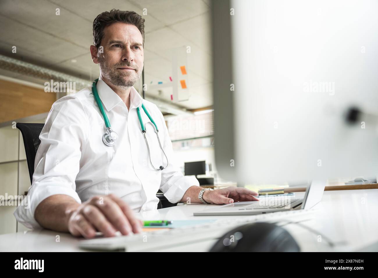 Confident doctor using computer at desk in office Stock Photo