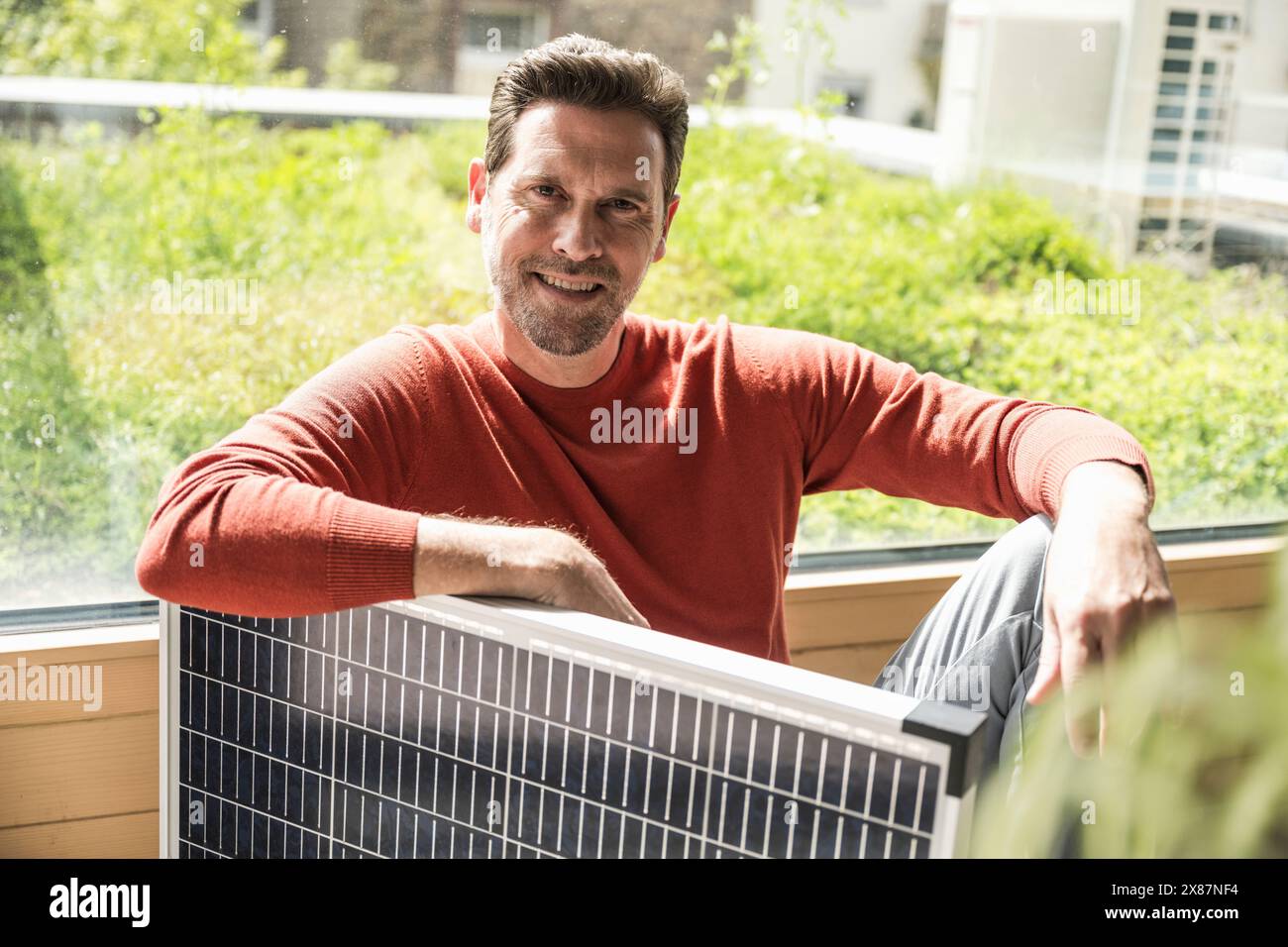 Confident mature businessman sitting with solar panel in office Stock Photo