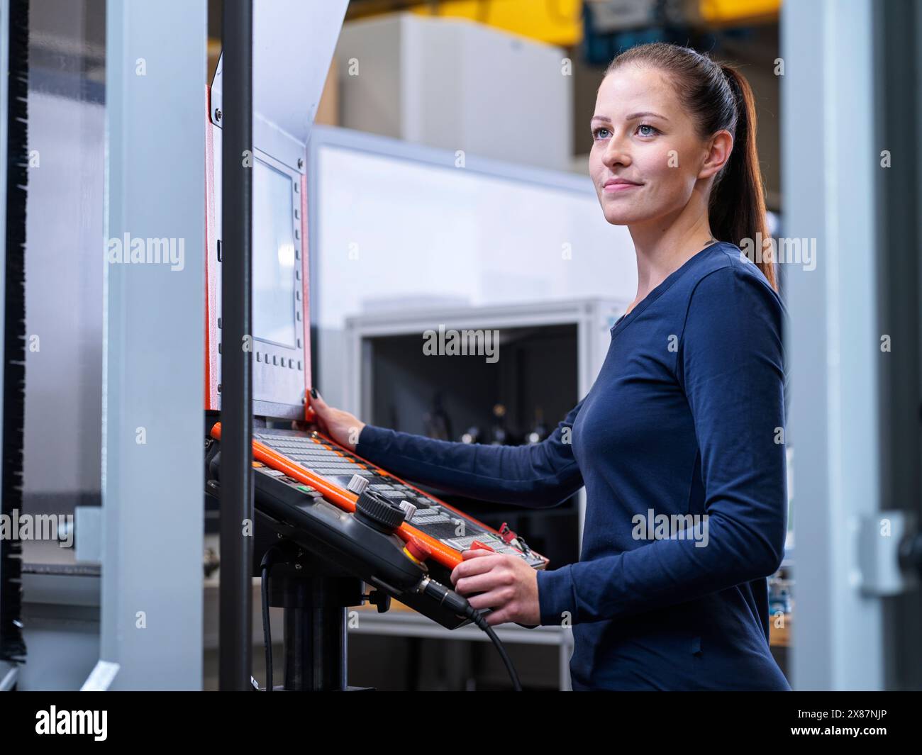 Smiling engineer standing near CNC machine panel at factory Stock Photo