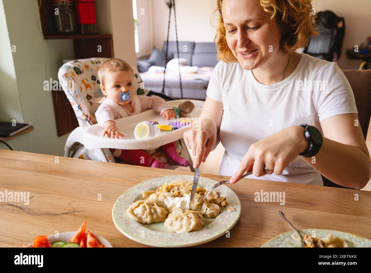 Smiling woman eating meal sitting next to daughter at home Stock Photo