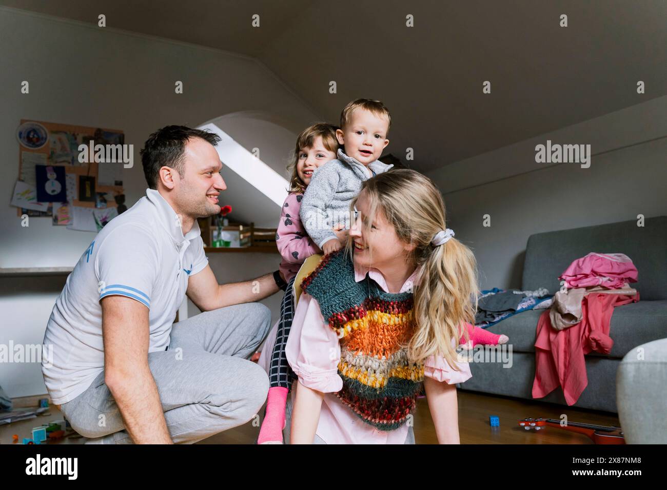 Smiling man by children on mother's back in living room Stock Photo
