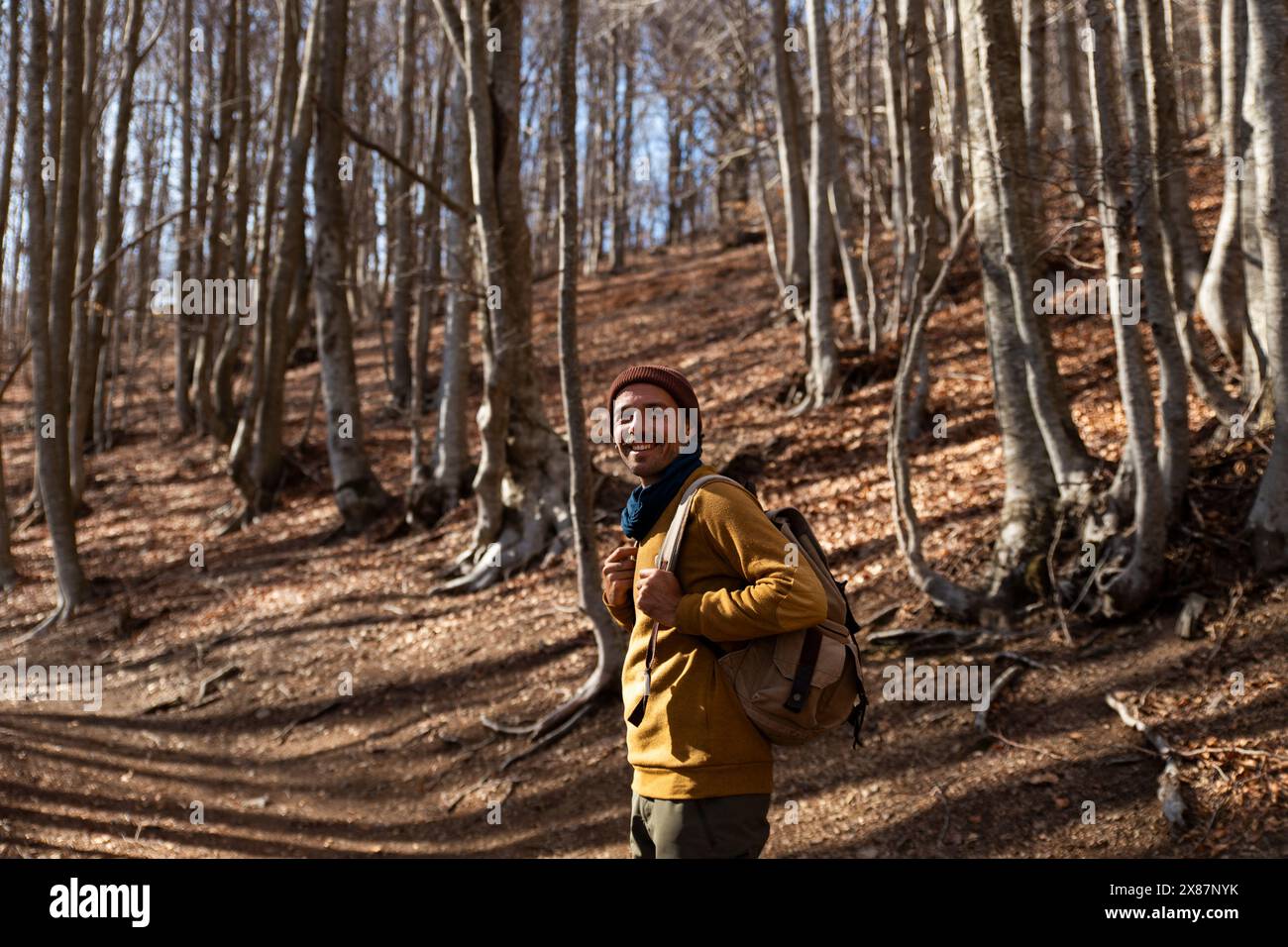 Smiling man with backpack standing in forest Stock Photo