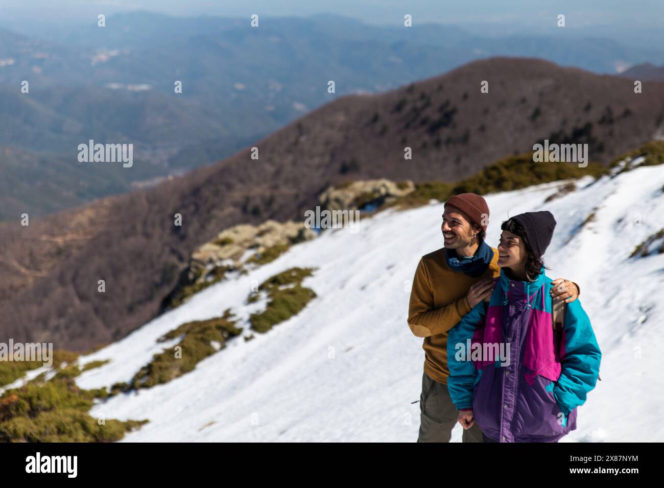Smiling man standing with arms around woman on snowy mountain Stock Photo