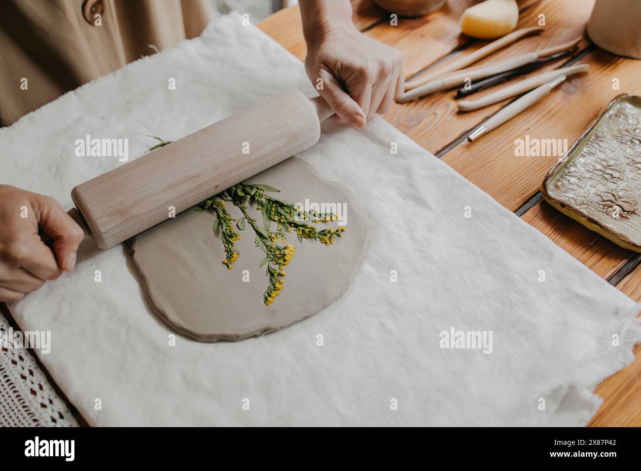 Hands of woman imprinting flowers on clay with rolling pin at home Stock Photo