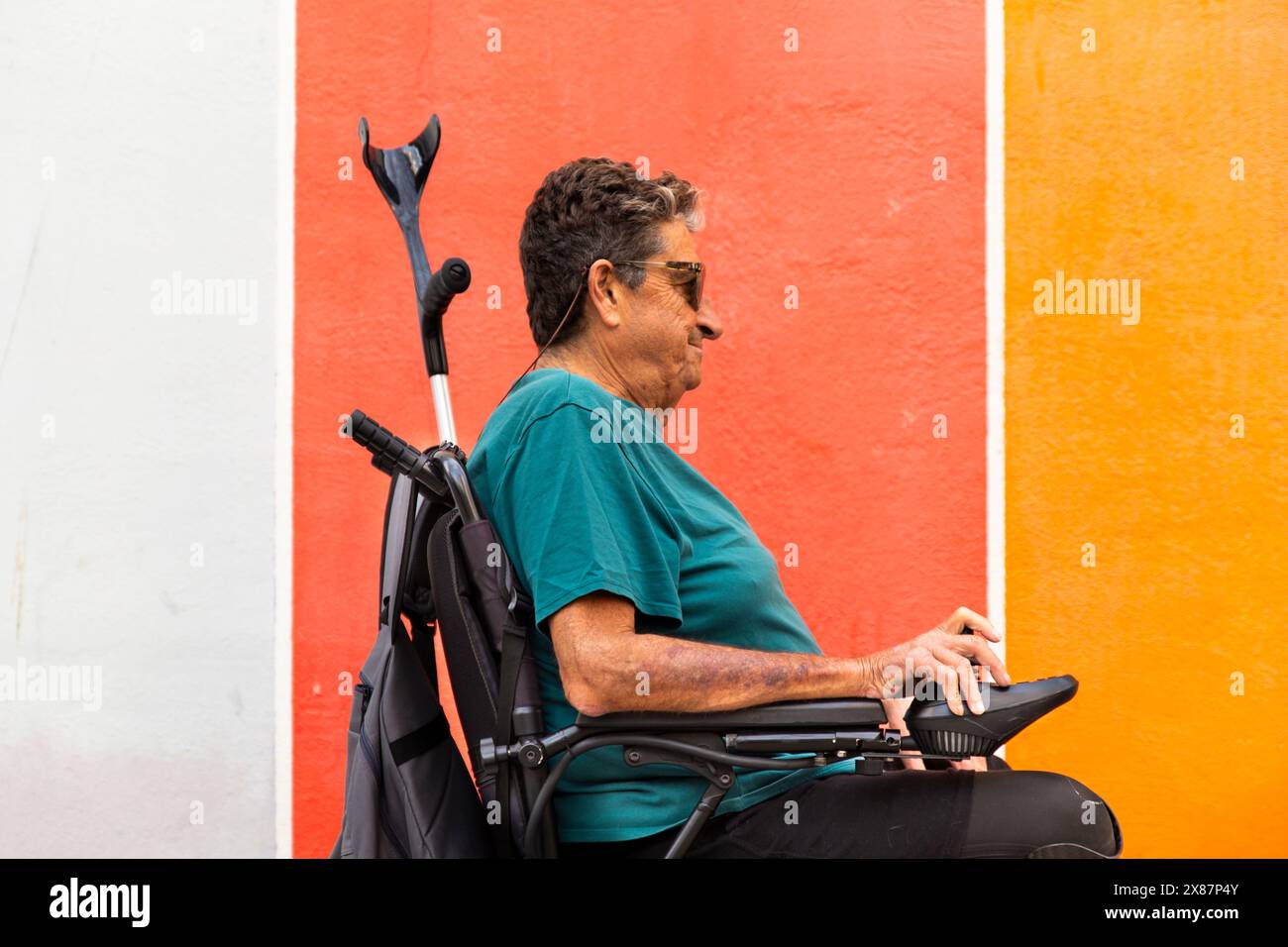 Disabled senior man in motorized wheelchair by colorful wall Stock Photo