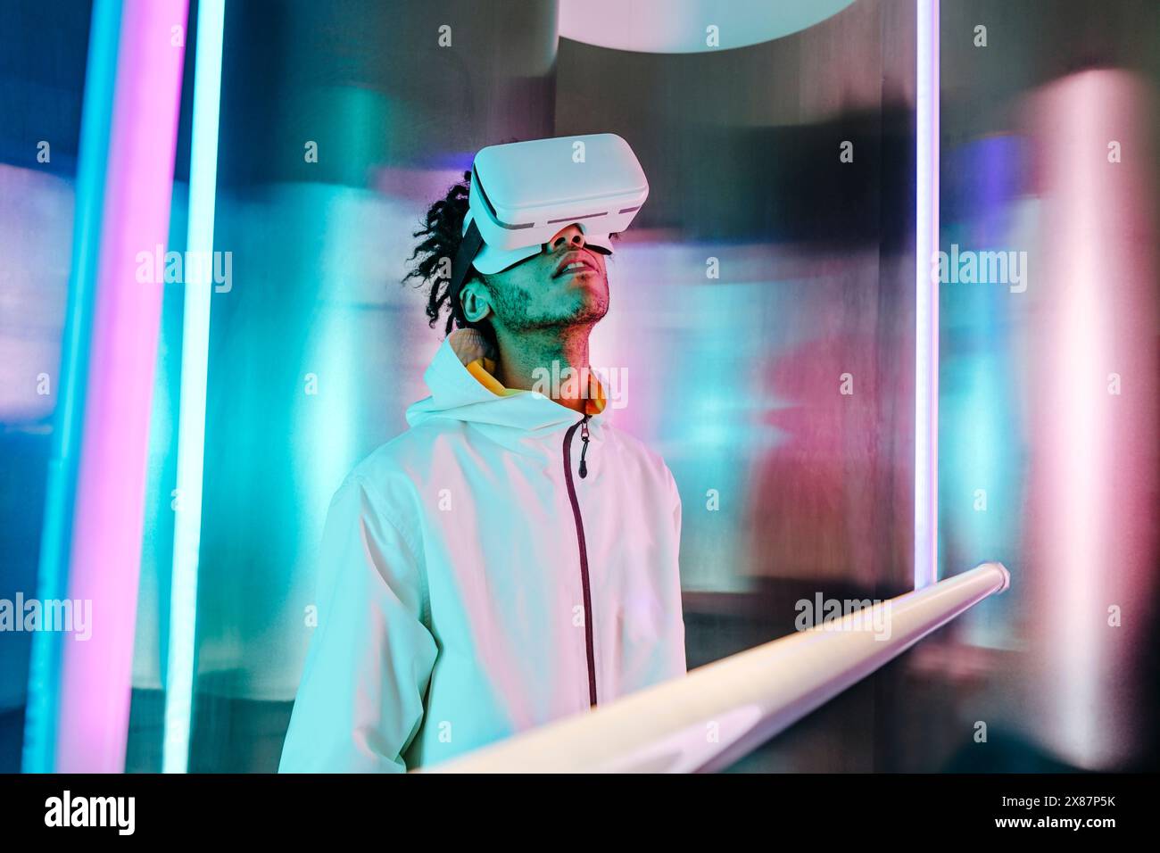 Man looking up wearing virtual reality headset near illuminated wall Stock Photo