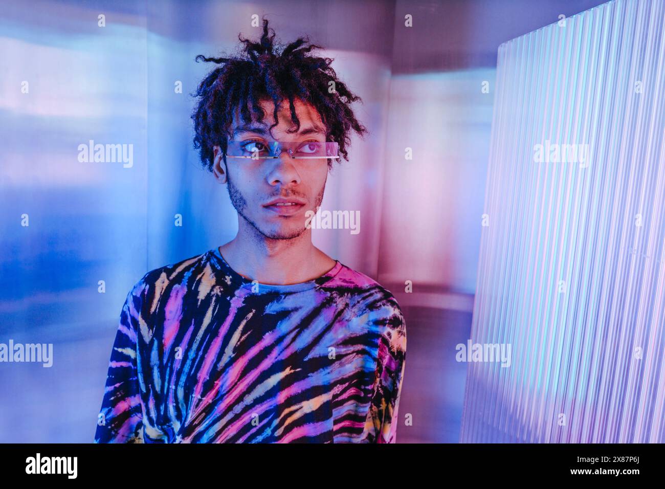 Thoughtful young man in sunglasses near illuminated wall Stock Photo