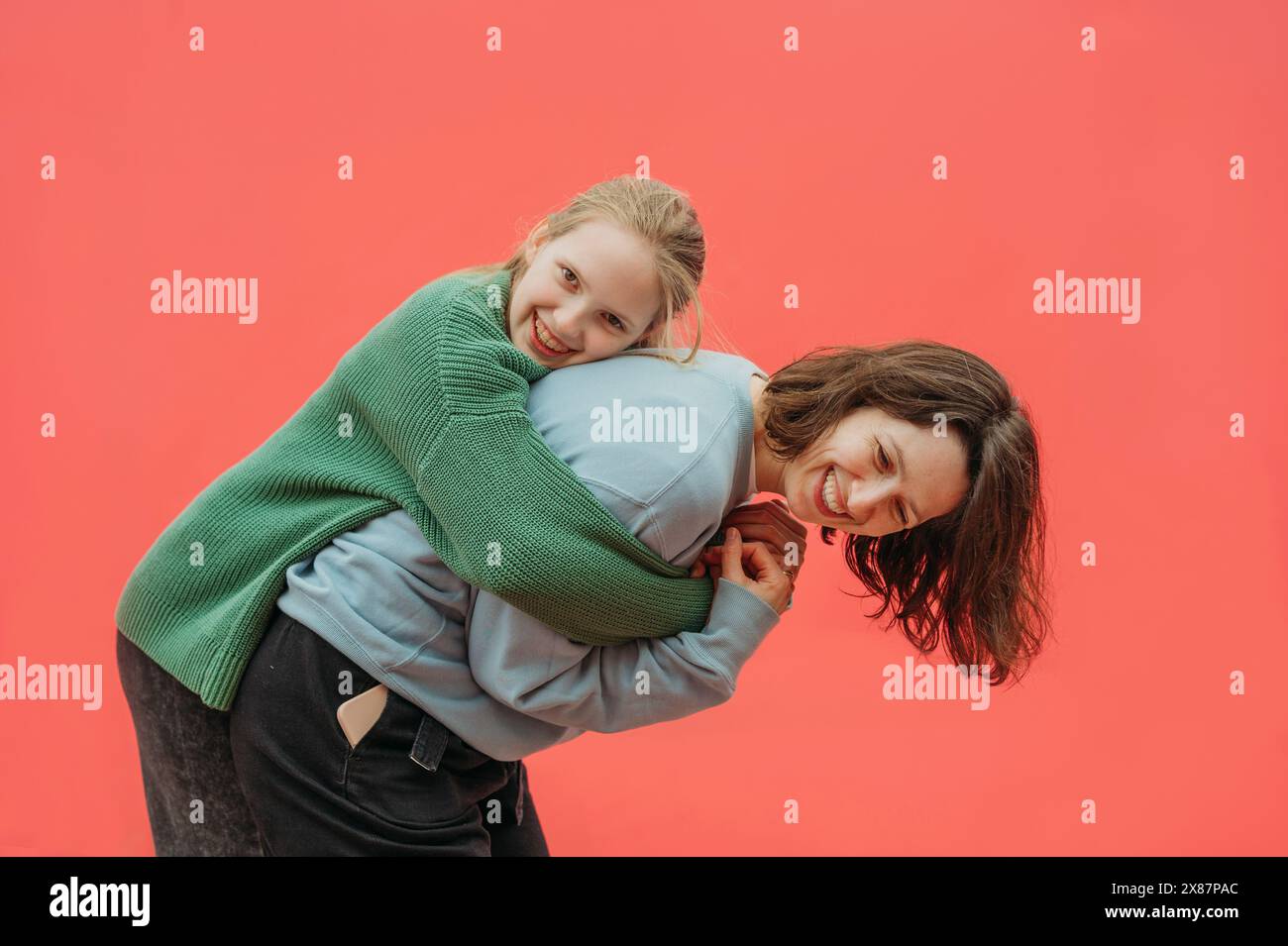 Daughter embracing mother against red background Stock Photo