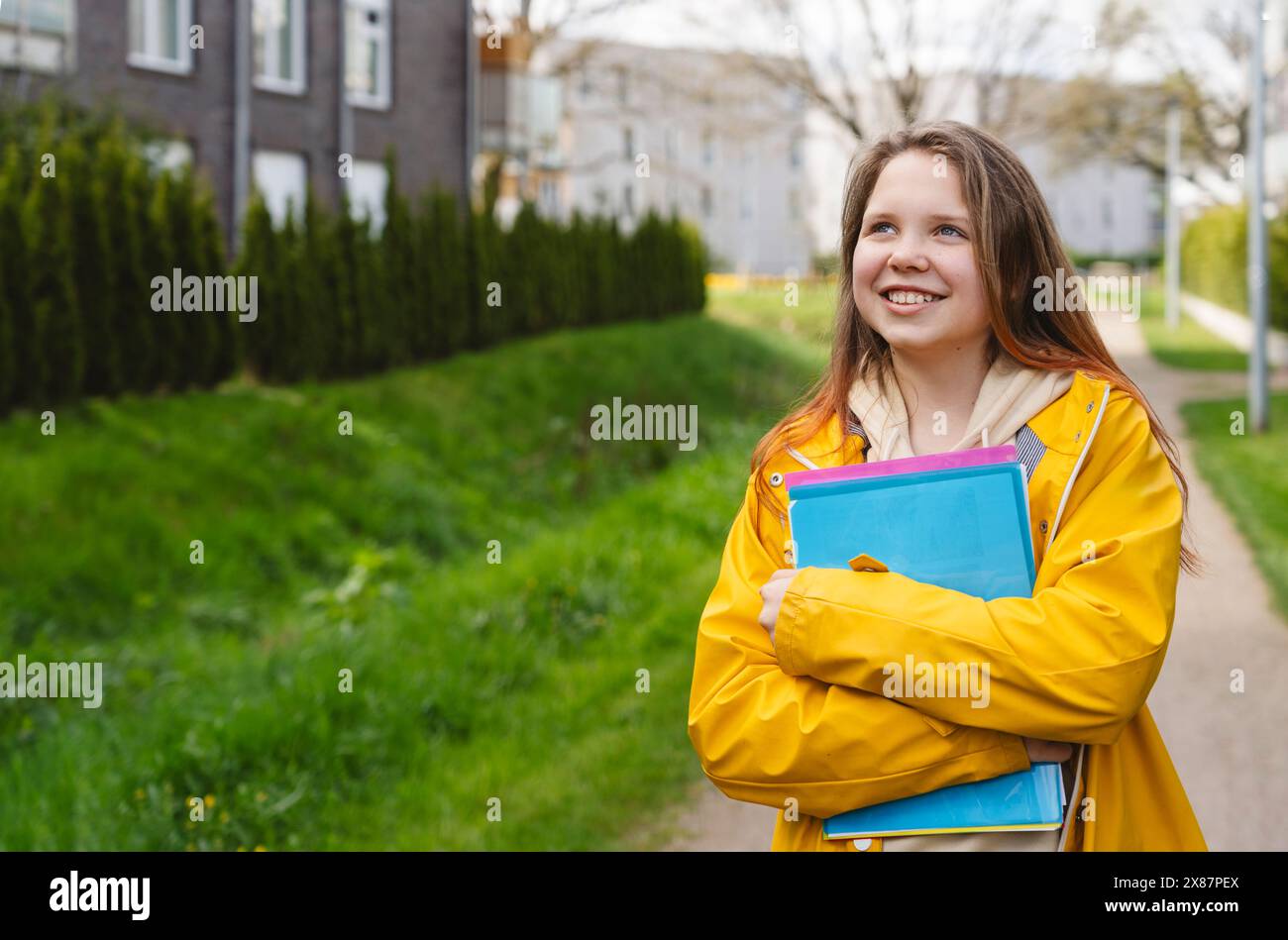 Smiling girl holding folders and standing on footpath Stock Photo