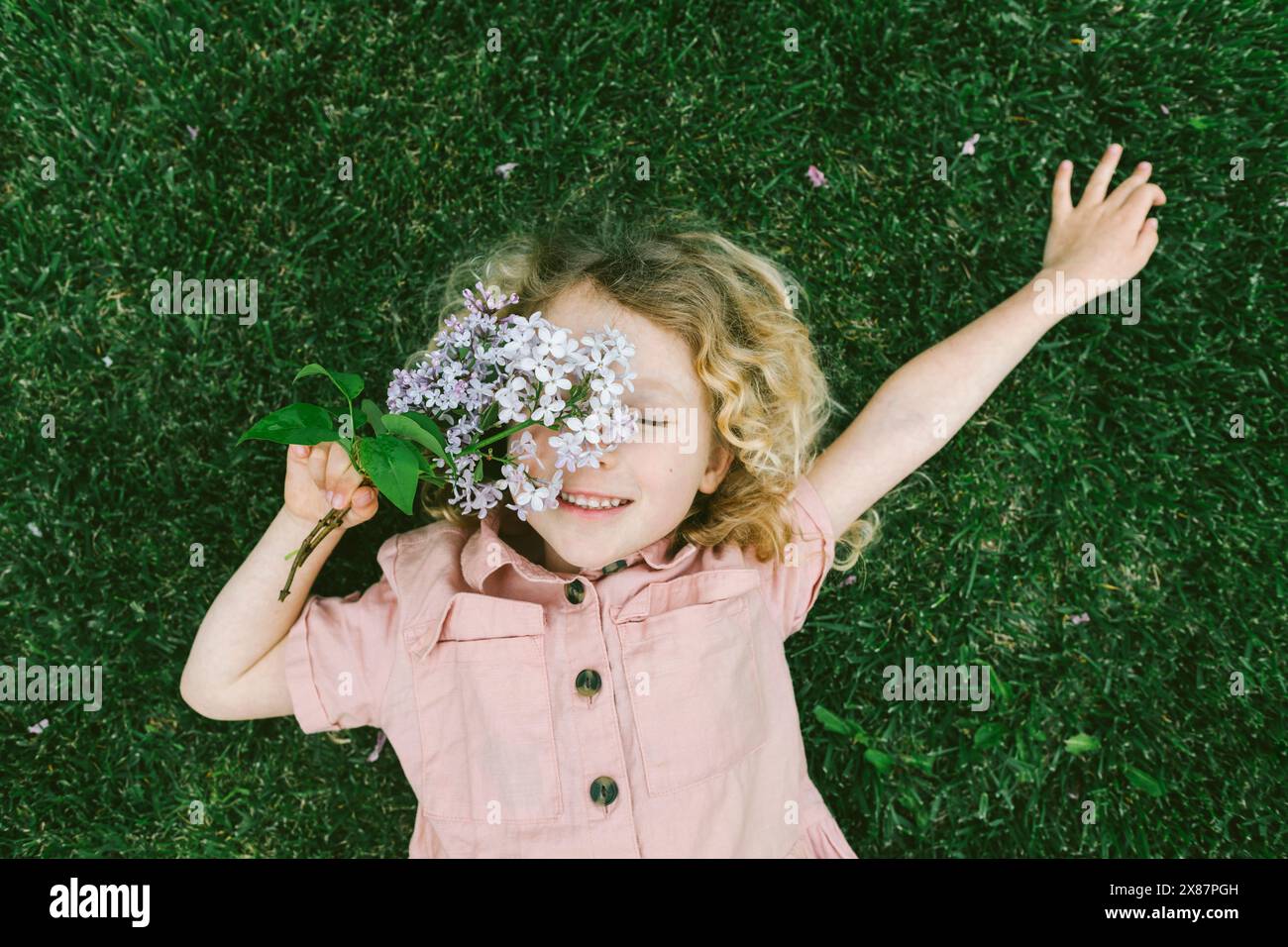Smiling girl lying on grass with lilac flowers at park Stock Photo - Alamy