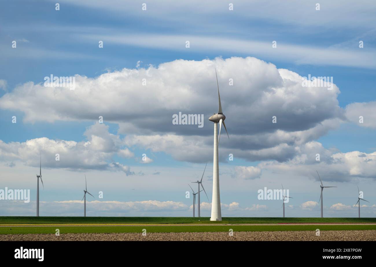 Wind turbines at field on sunny day under cloudy sky Stock Photo