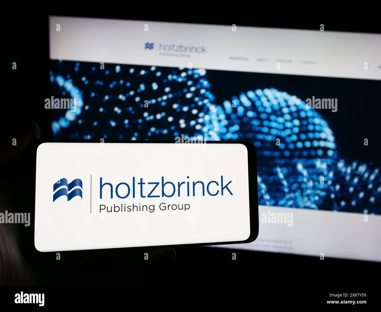 Person holding smartphone with logo of German media company Holtzbrinck Publishing Group in front of website. Focus on phone display. Stock Photo