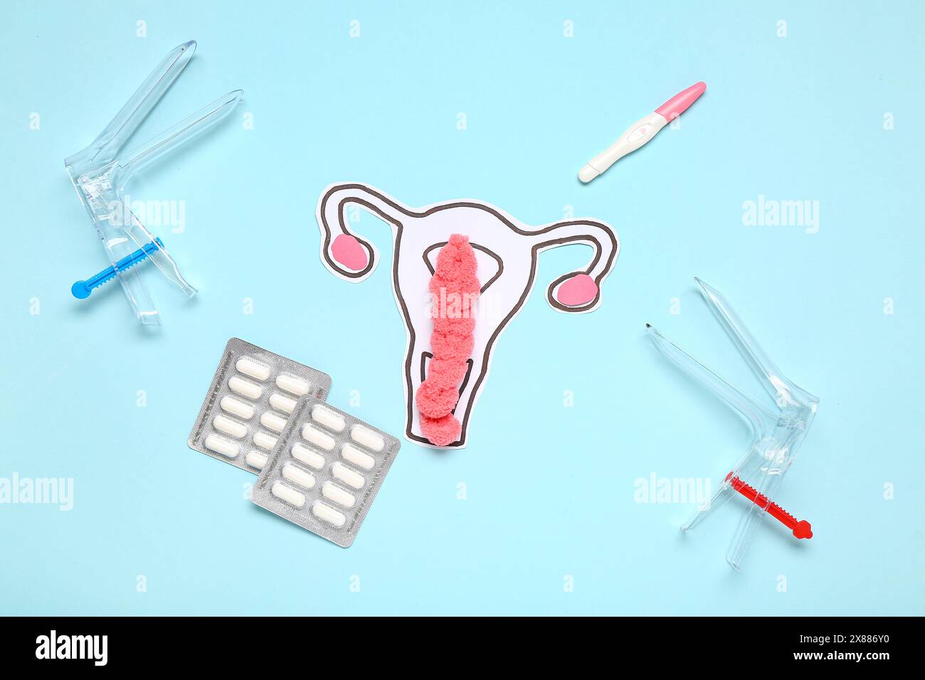 Paper uterus with gynecological speculums, pills and pregnancy test on
