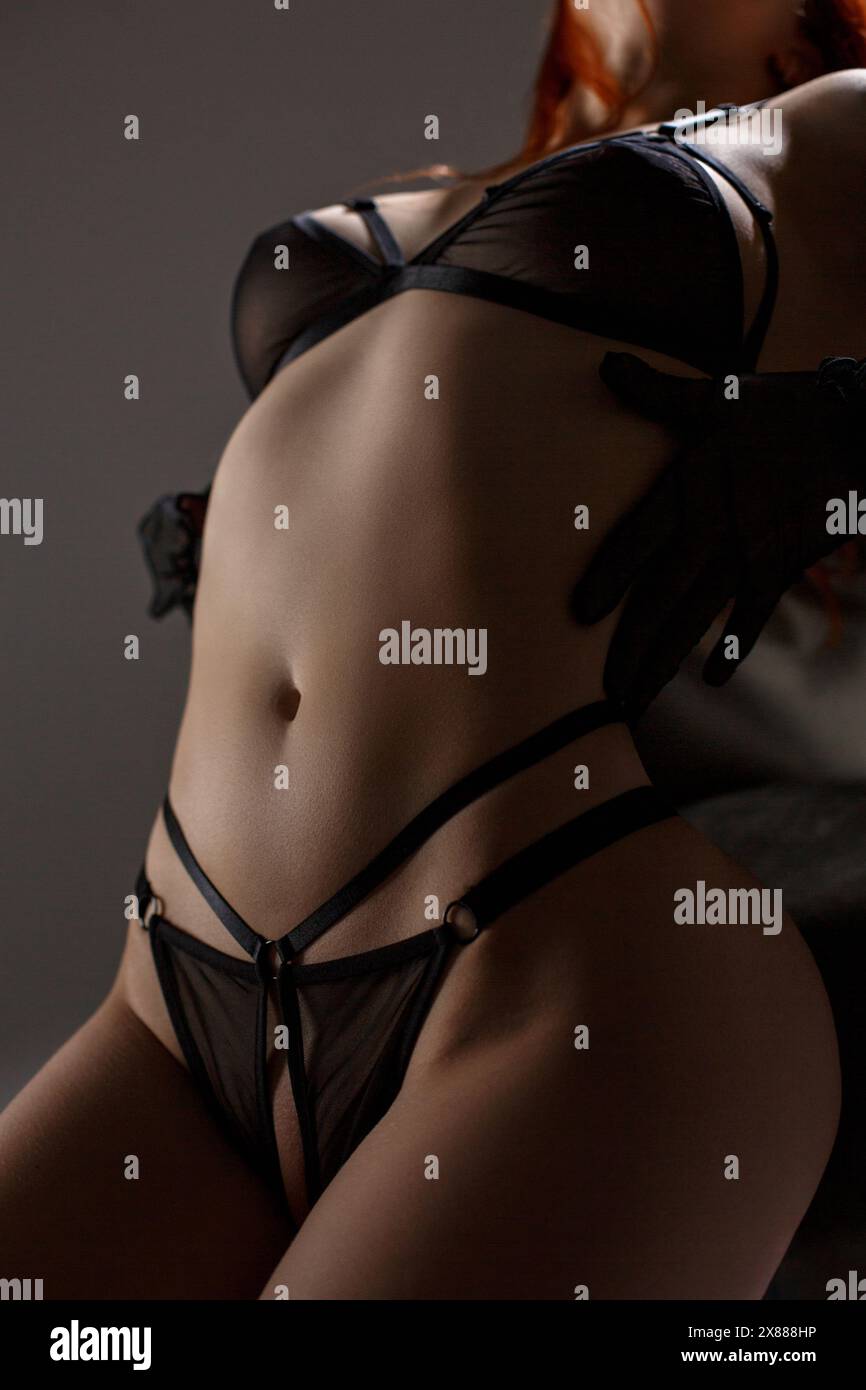 Close up of a young sexy redhead woman in see-through black lingerie  leaning on a chair in studio lights and attractively posing with hands in  black g Stock Photo - Alamy