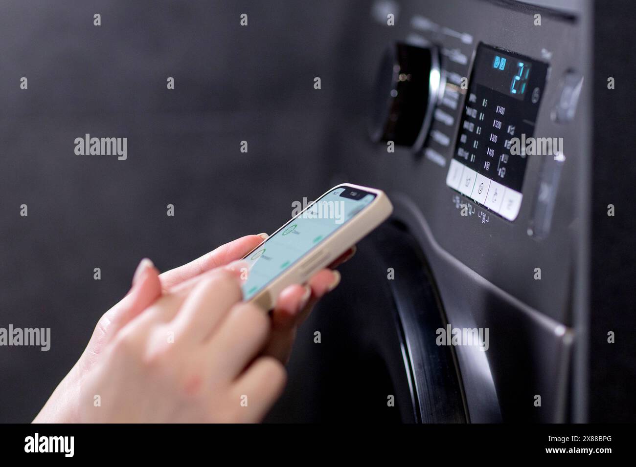 Woman controls washing machine with a phone. Stock Photo
