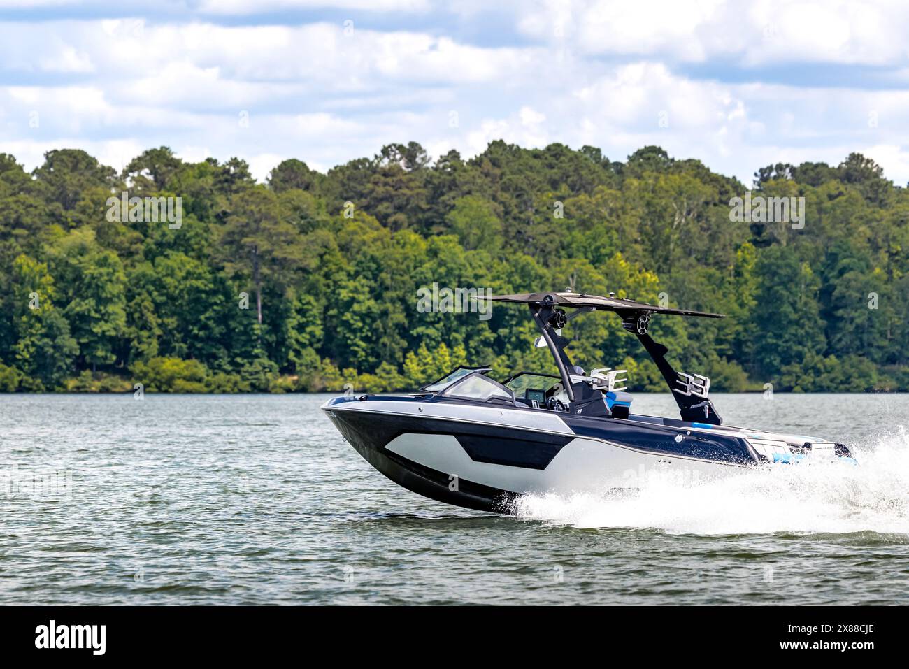 Boater on blue wakeboard wake boat enjoying summer day on freshwater lake. Stock Photo
