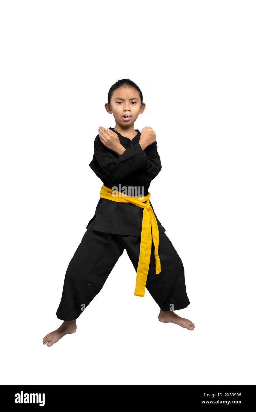 Determined young girl in a black karate gi with a yellow belt stands in a defensive pose, showcasing her martial arts stance against a white backgroun Stock Photo