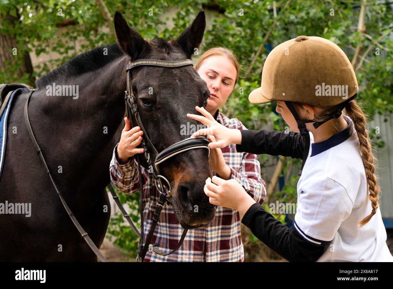 Woman and young rider girl carefully adjusting the bridle on a black