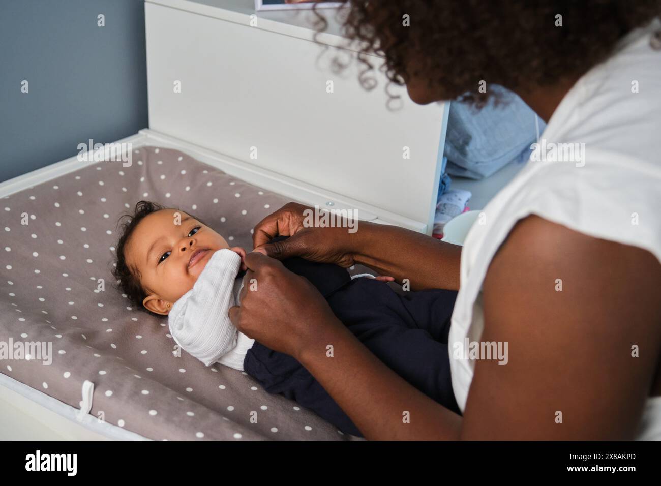 African mother is dressing up her baby girl on a changing table. Stock Photo