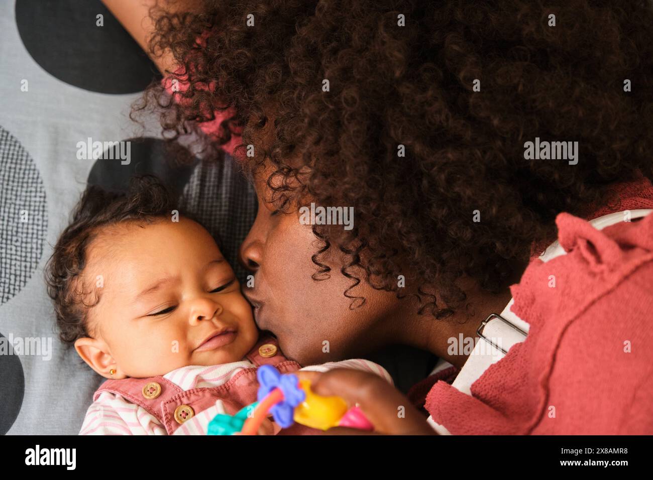 African woman is kissing a baby girl laying in bed. Stock Photo