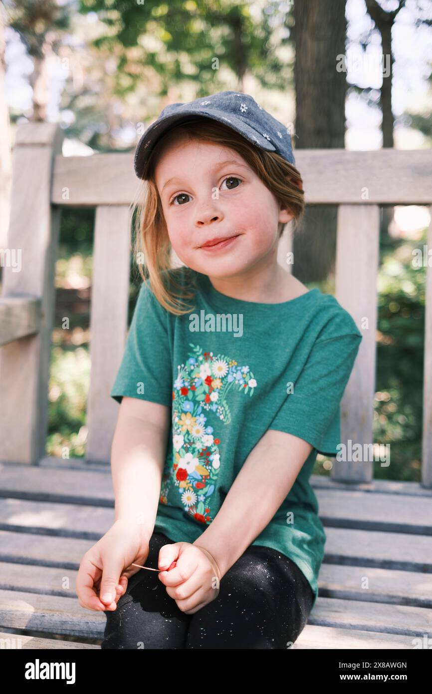 Portrait of a cute young girl sitting on a bench outdoors Stock Photo