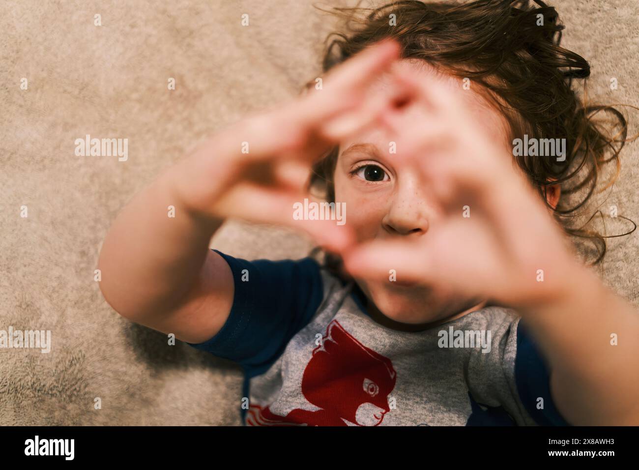 Child lying on carpet making hand heart gesture Stock Photo