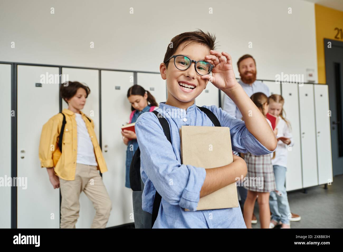 A boy in a blue shirt and glasses stands confidently in front of lockers in a school hallway. Stock Photo