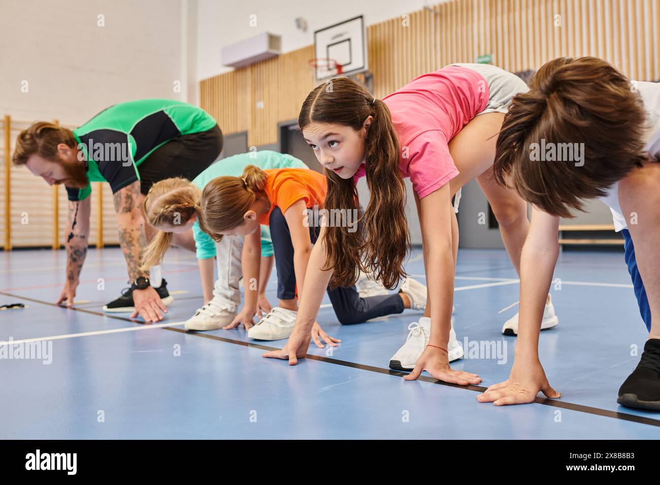 A man teacher stands atop a vibrant blue floor, surrounded by a diverse group of children. The classroom exudes brightness and liveliness. Stock Photo