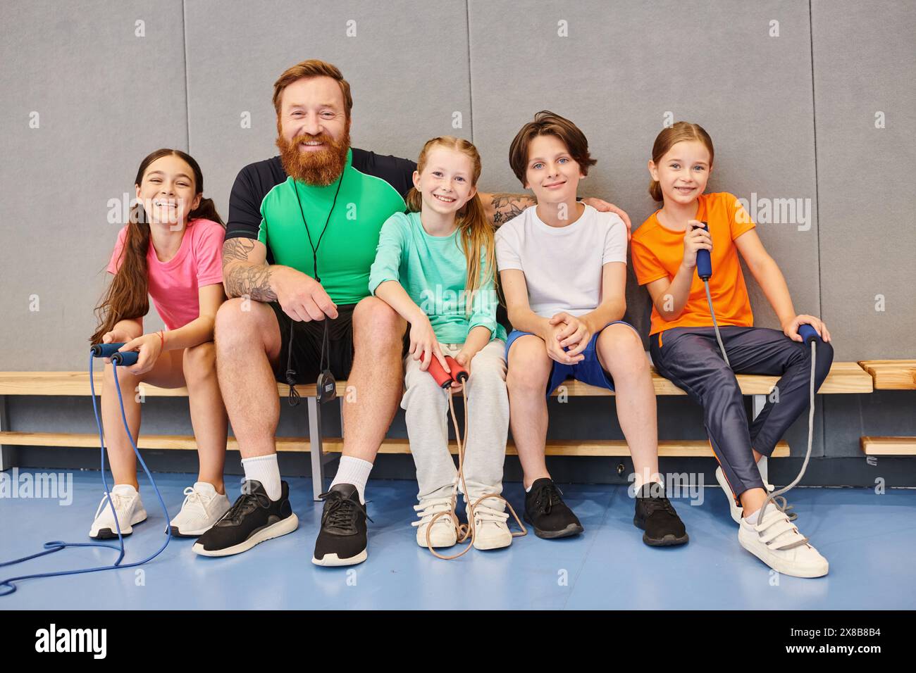 A man with a beard, a teacher, sitting on a bench surrounded by happy, diverse children of various ages, engaging in conversation and learning togethe Stock Photo