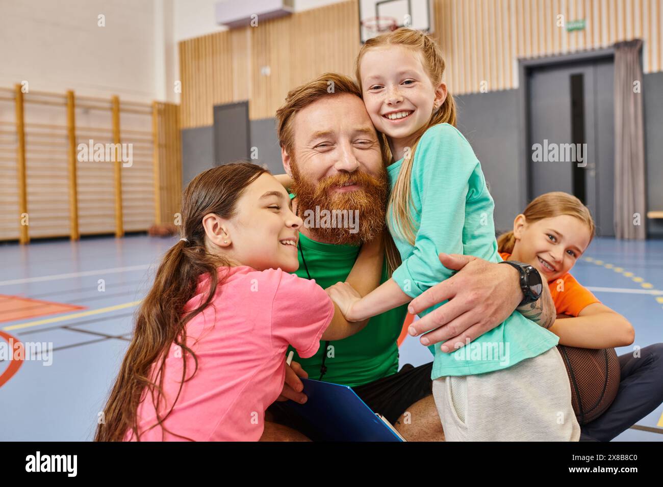 A bearded teacher with open arms, warmly hugging a diverse group of children in a vibrant classroom setting filled with laughter and joy. Stock Photo