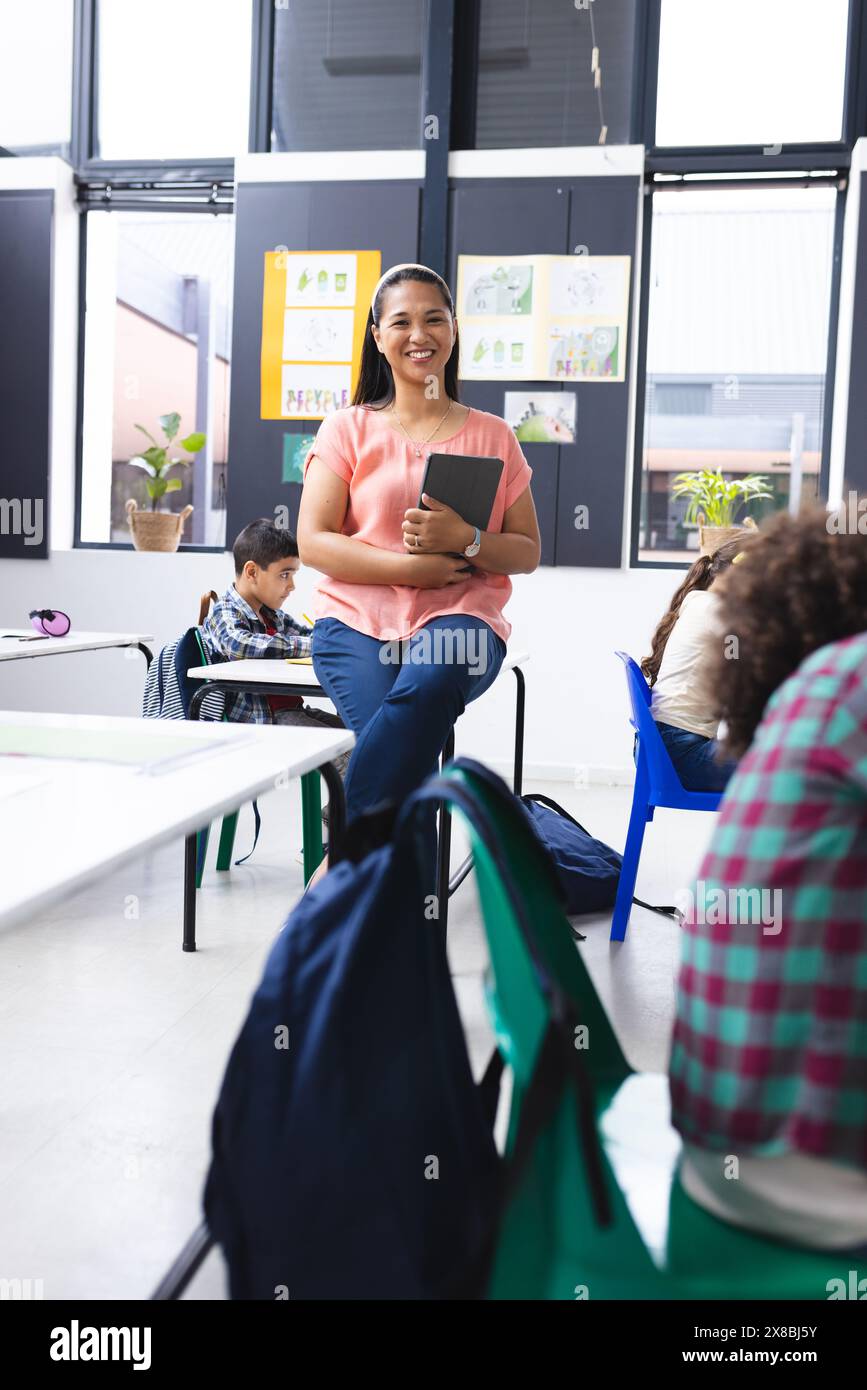 In school, young biracial female teacher holding a tablet smiles in the ...