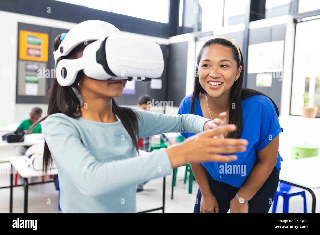 In school, middle-aged biracial teacher guides a young biracial student using VR in the classroom Stock Photo