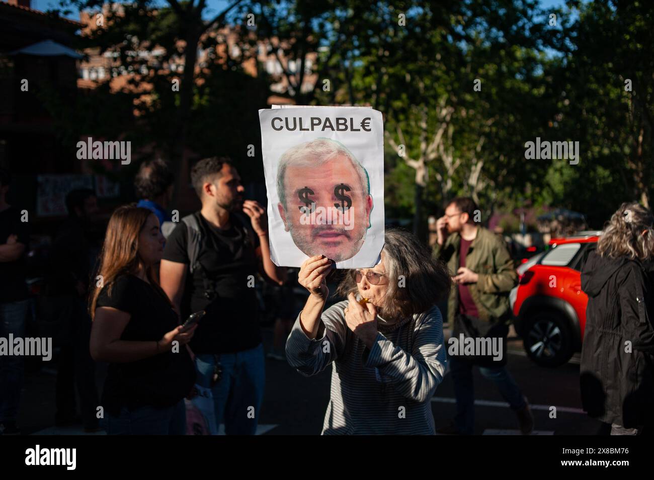 In the Park Guell neighborhood of Barcelona a woman holds a placard with the face of the city's mayor Jaume Collboni and 'guilty' written. Barcelona residents gathered around Park Guell in Barcelona against the Louis Vuitton fashion show and protesting various social issues such as mass tourism, gentrification, animal rights or the commercialization and privatization of public spaces by the city council. Stock Photo