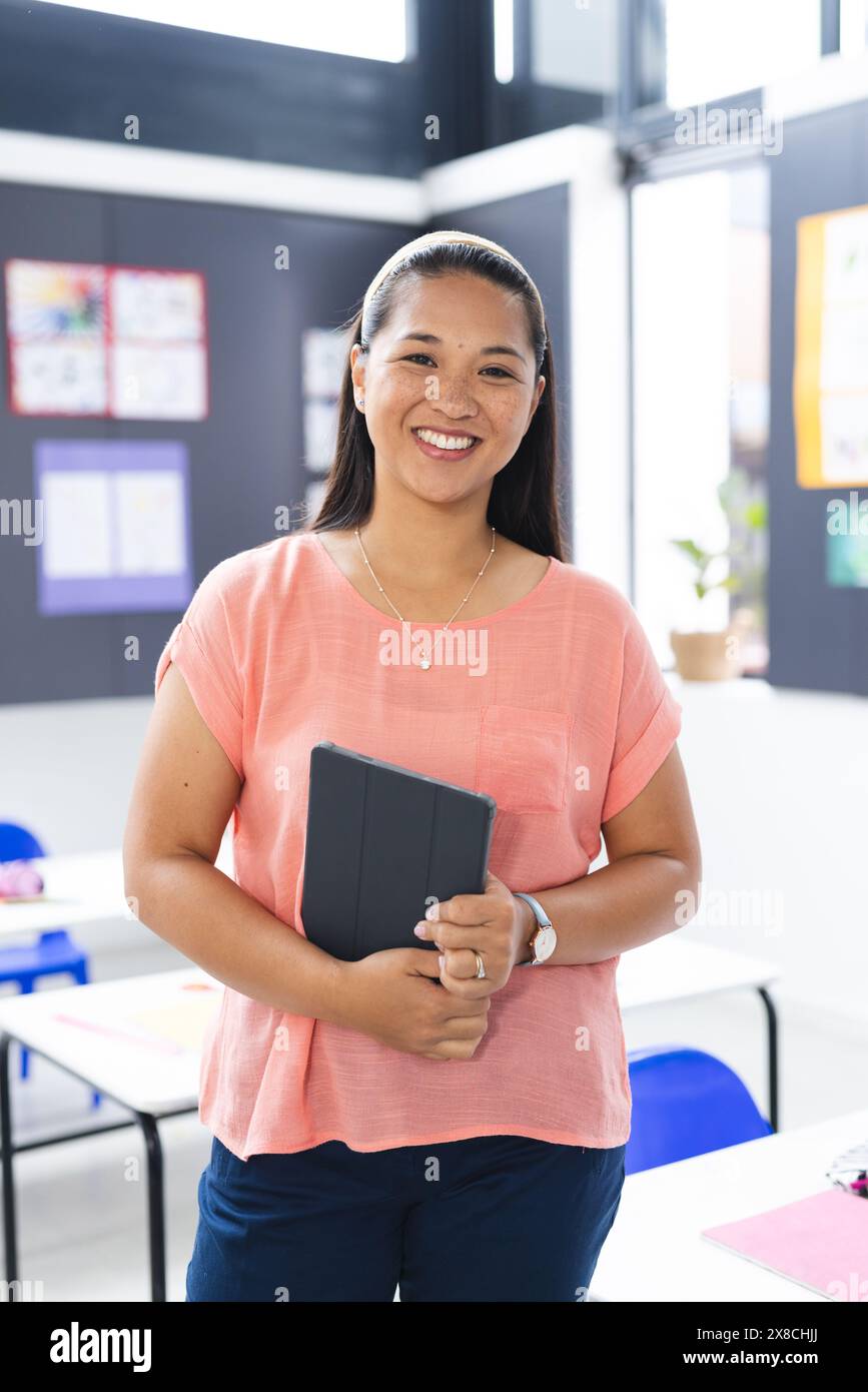 In school, young biracial female teacher holding a tablet in the ...