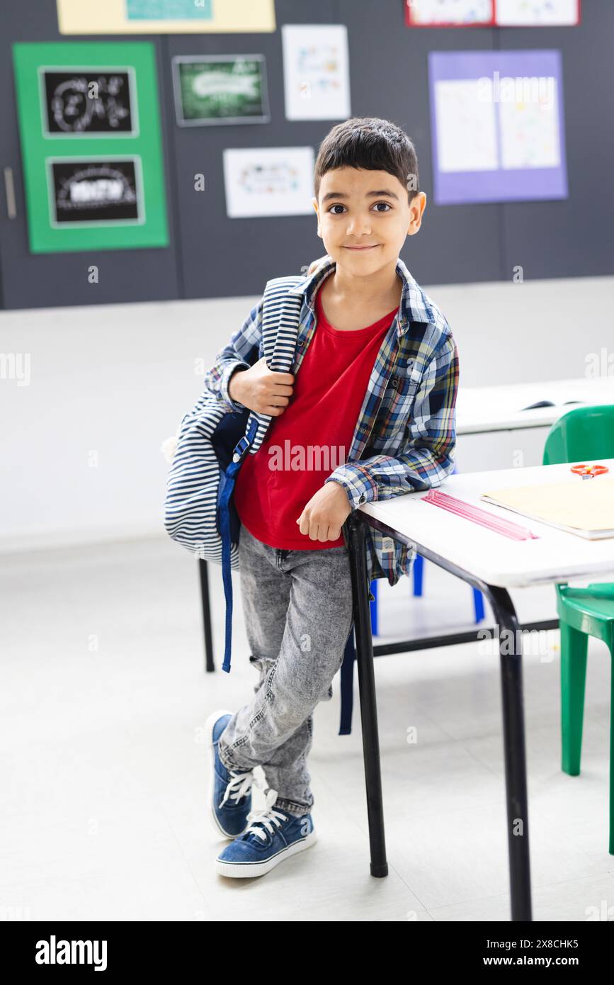 In school, young biracial boy with a backpack stands by a desk in the ...