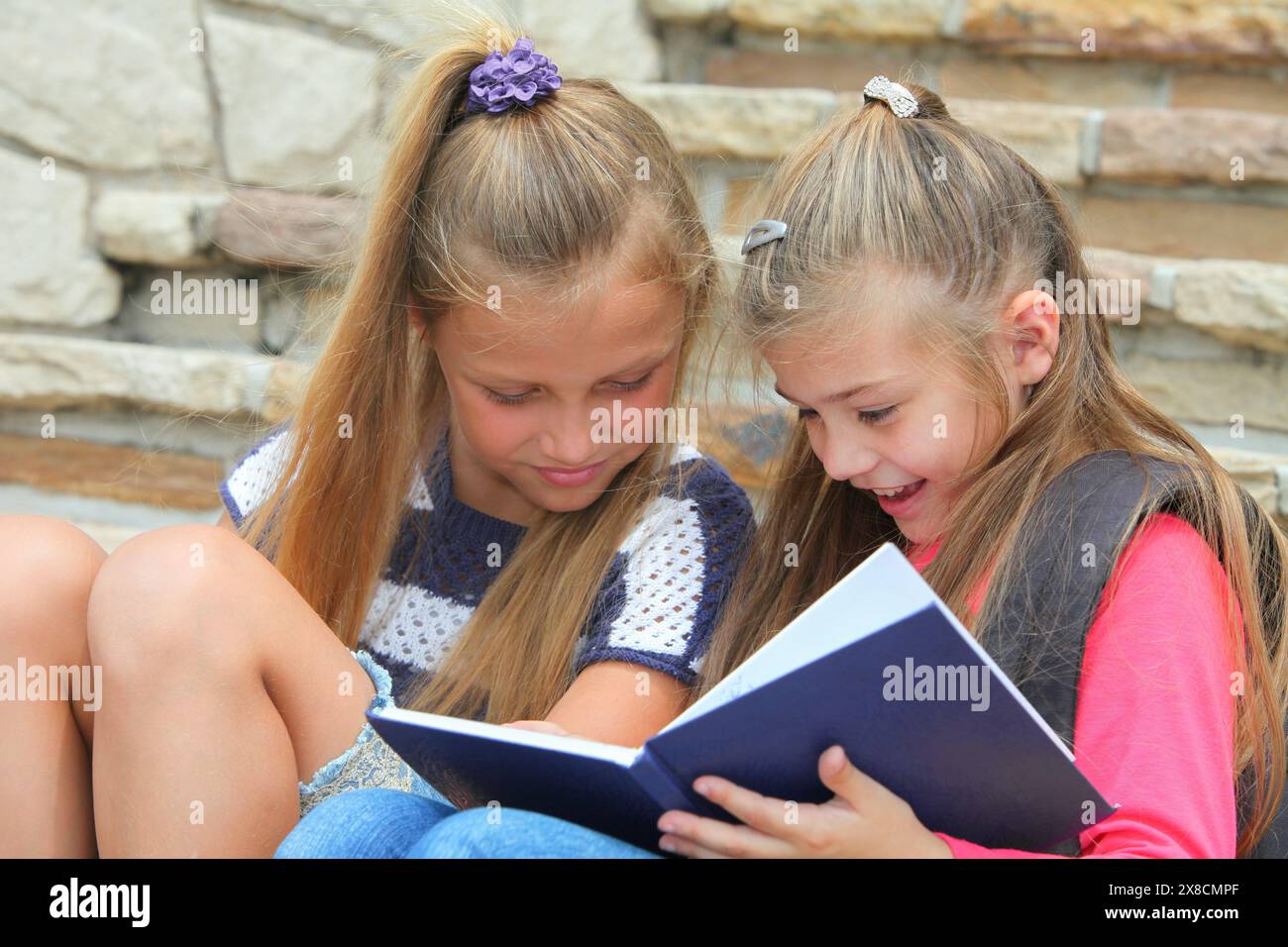 cheerful elementary  school girls reeding notebook studying sitting on stairs Stock Photo