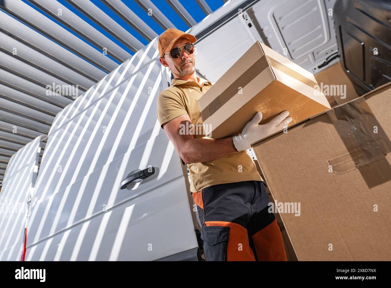 Caucasian courier standing next to delivery van while holding a box in his hand. Stock Photo