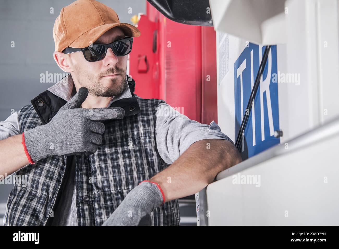 Truck driver wearing a hat and gloves is showing TIR sign hanged on a semi truck trailer Stock Photo