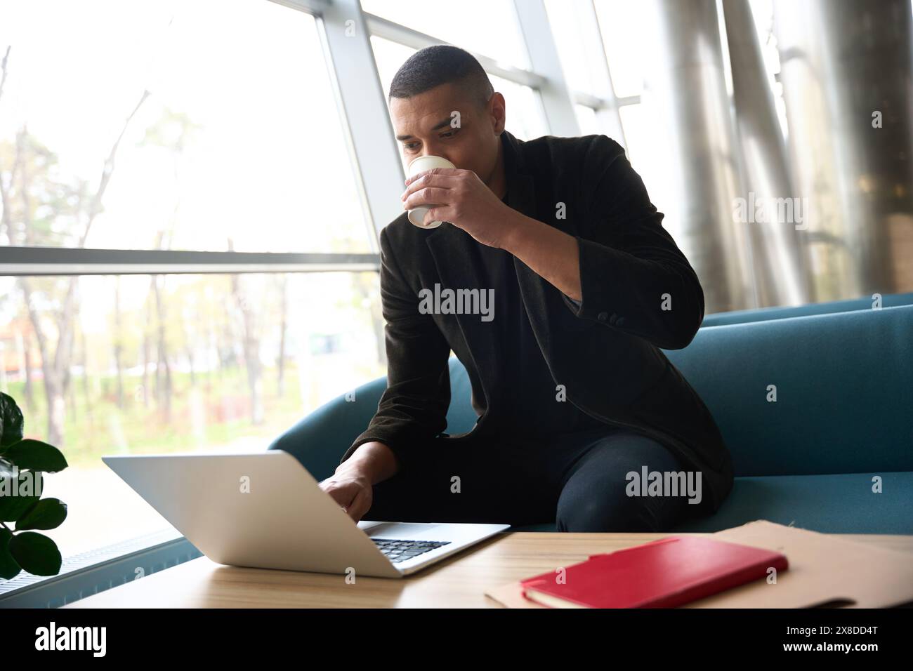 Young freelancer sitting and working on laptop while drinking coffee Stock Photo