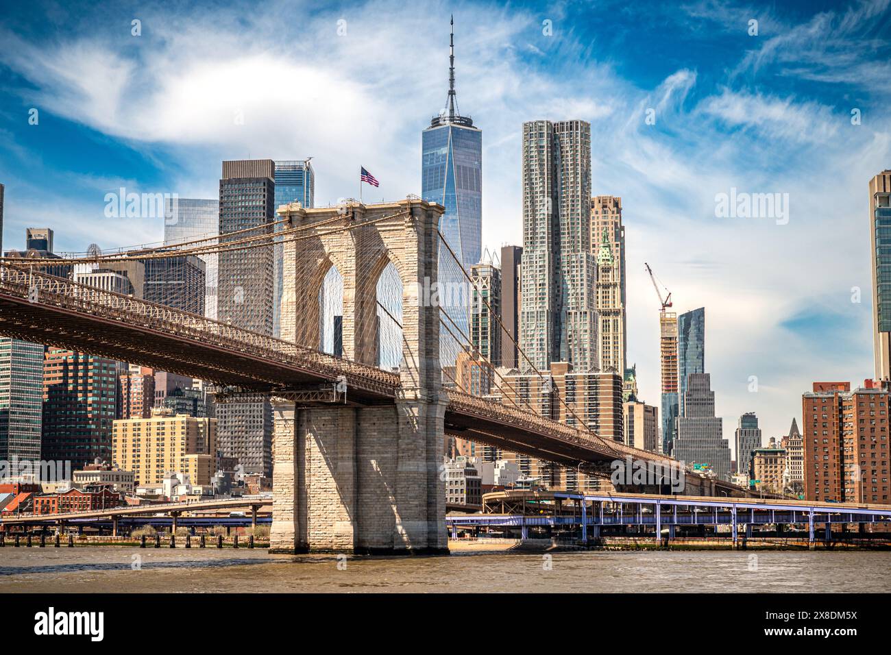 Majestic Brooklyn Bridge graces the NYC skyline. Soaring steel arches frame the cityscape, bathed in warm sunlight. Iconic landmark for travel . Stock Photo