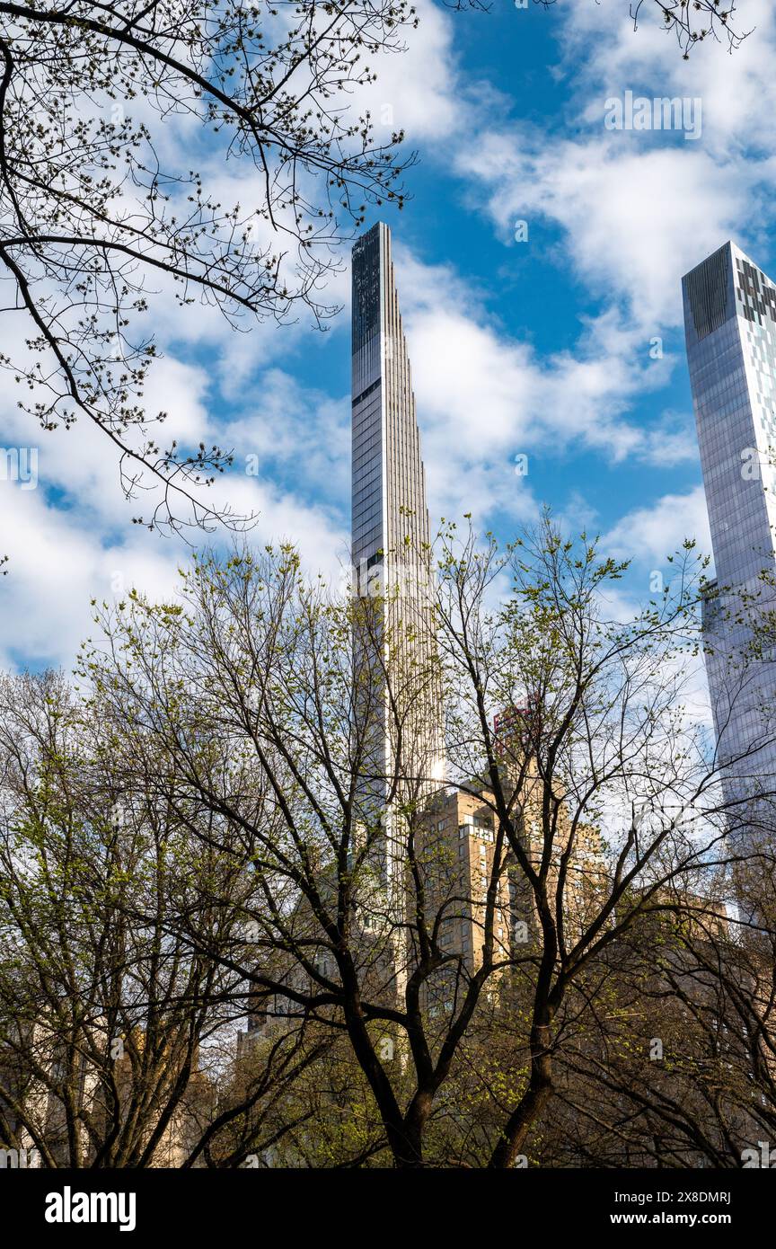 NYC's Art Deco gem basks in sunshine! Steinway Tower rises above lush greenery in Central Park in a sunny day and some trees in the foreground. Stock Photo