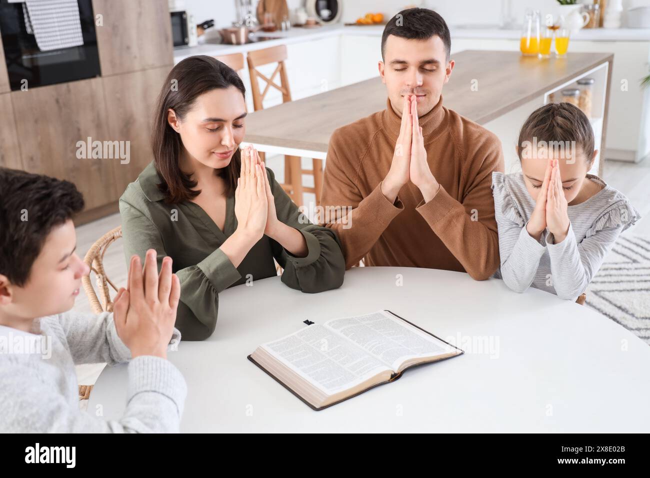 Family praying with Holy Bible on table in kitchen Stock Photo