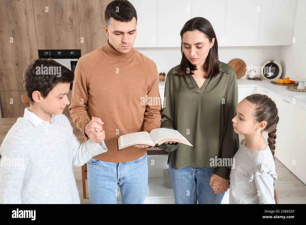 Family with Holy Bible praying together in kitchen Stock Photo