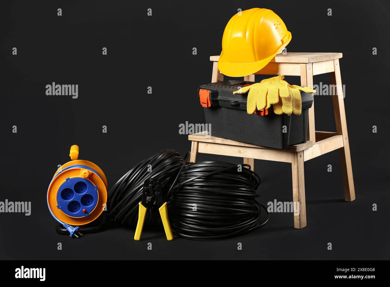 Stepladder with electrician tools, rolled cables and hardhat on black background Stock Photo