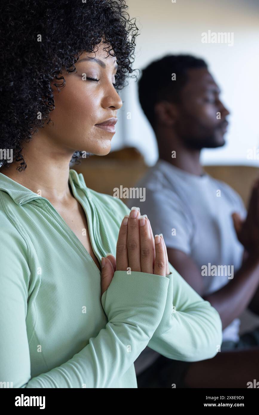 A diverse couple meditating at home, both sporting curly hair Stock Photo